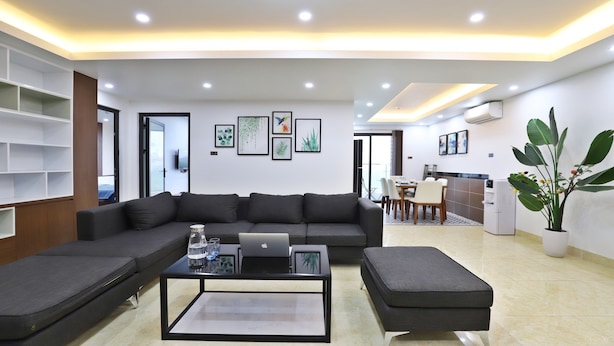A modern living room with a sectional sofa, a coffee table with a laptop, and a dining area with chairs and a table. - Paradise Home Xuan La (Hanoi)