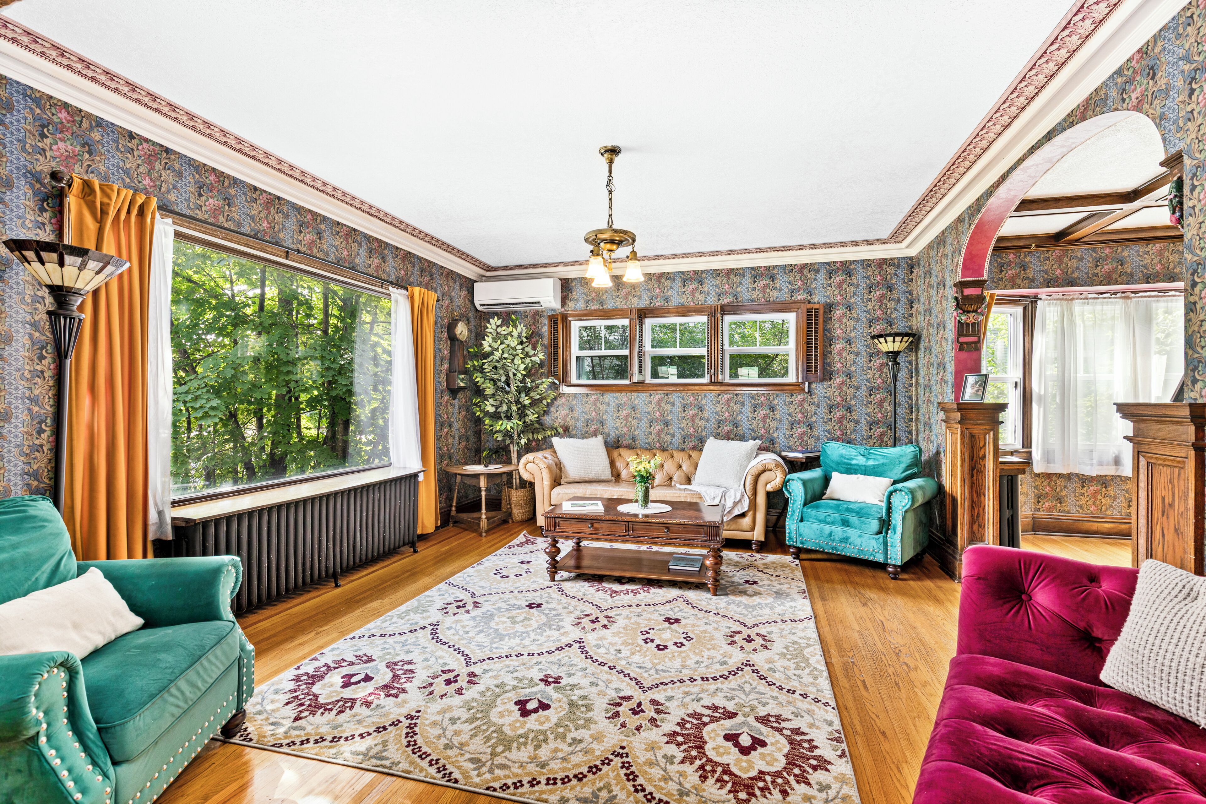 Een klassieke woonkamer met een groot raam, een open haard en diverse zithoeken.