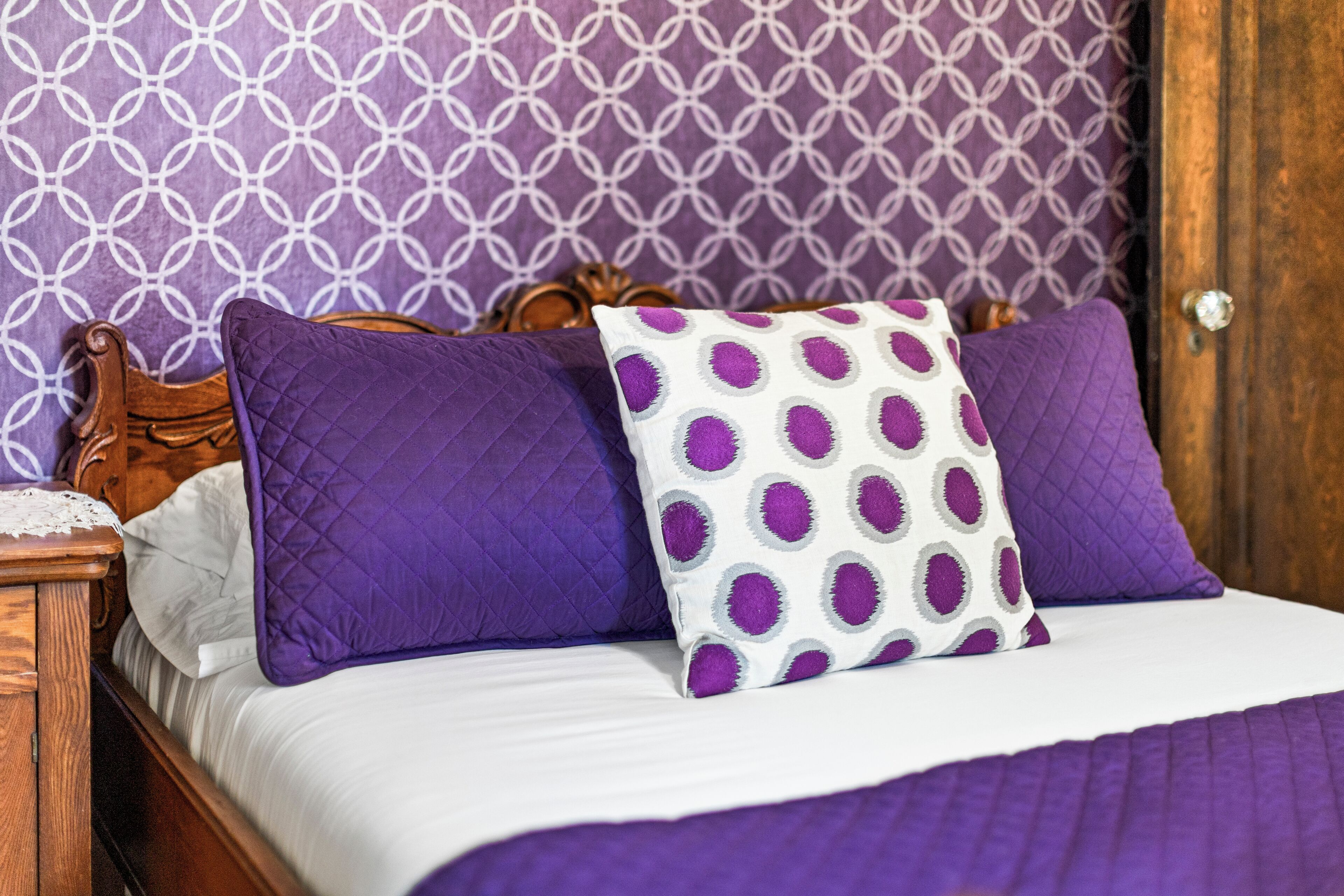 Ein Bett mit einer weißen und violetten Steppdecke, zwei violetten Kissen und einem weißen Kissen mit violetten Punkten.