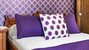 Ein Bett mit einer weißen und violetten Steppdecke, zwei violetten Kissen und einem weißen Kissen mit violetten Punkten.