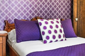 A bed with a white and purple quilt, two purple pillows, and a white pillow with purple polka dots.