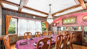 Ein Esszimmer mit großem Tisch, gedeckt für sechs Personen, Holzstühlen, einer Chandelierleuchtre und Blick ins Grüne.