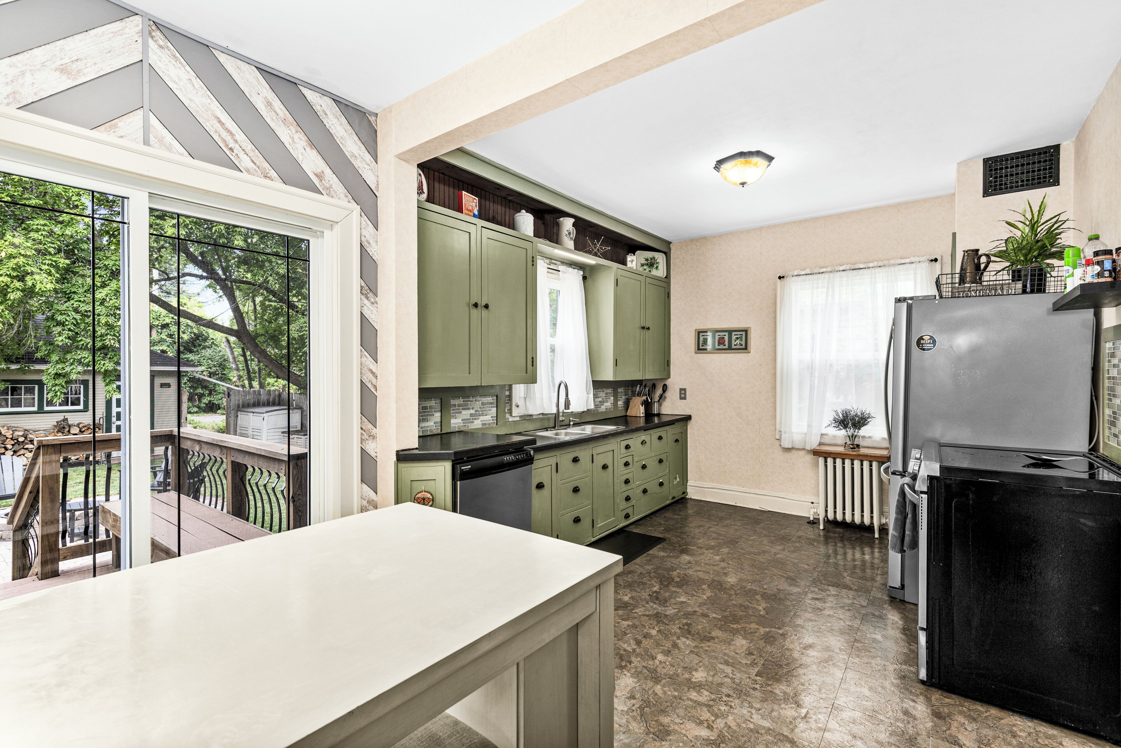Una cocina con lavavajillas, refrigerador y ventana con vista a un jardín.