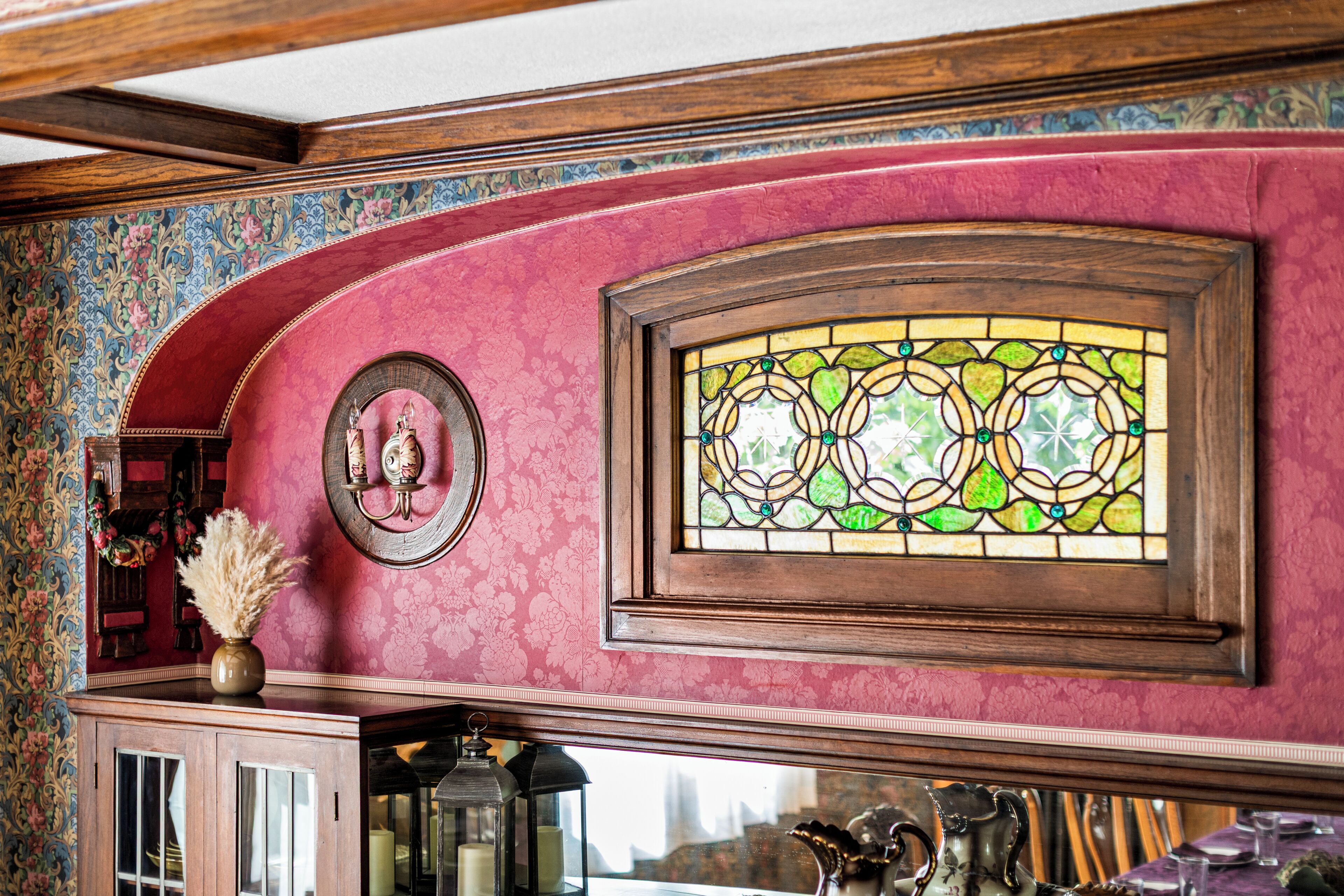 Une pièce dotée d’une grande fenêtre à vitraux, d’un meuble en bois et d’un papier peint à motifs floraux.