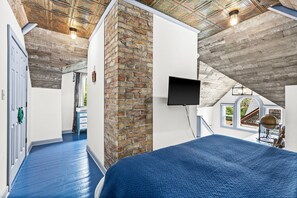 A room with a brick wall, a flat-screen TV mounted on the wall, and a blue patterned bedspread. - Leraan House. Historic home in Duluth/Superior (Superior)