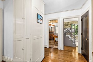 A hallway with wooden flooring, white walls, and a door leading to a room with a staircase.