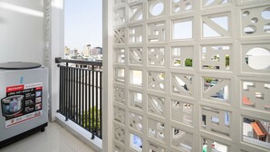 En balkong med en vit avskärmning som har geometriska utskärningar, ett kylskåp från Sharp och utsikt över stadsbilden.