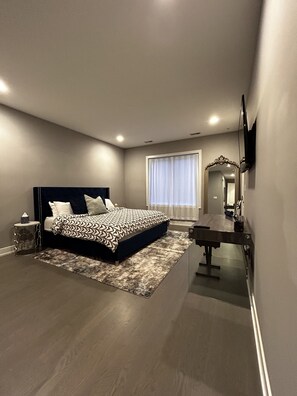 Relax in this serene bedroom with a large bed, nightstand, and dresser, plus a large window with sheer curtains.