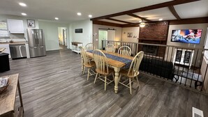 A spacious kitchen with modern appliances, a dining area with wooden chairs and a table, and a living area with a TV and fireplace.
