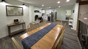 A spacious living area with a wooden dining table, chairs, and a kitchen in the background.