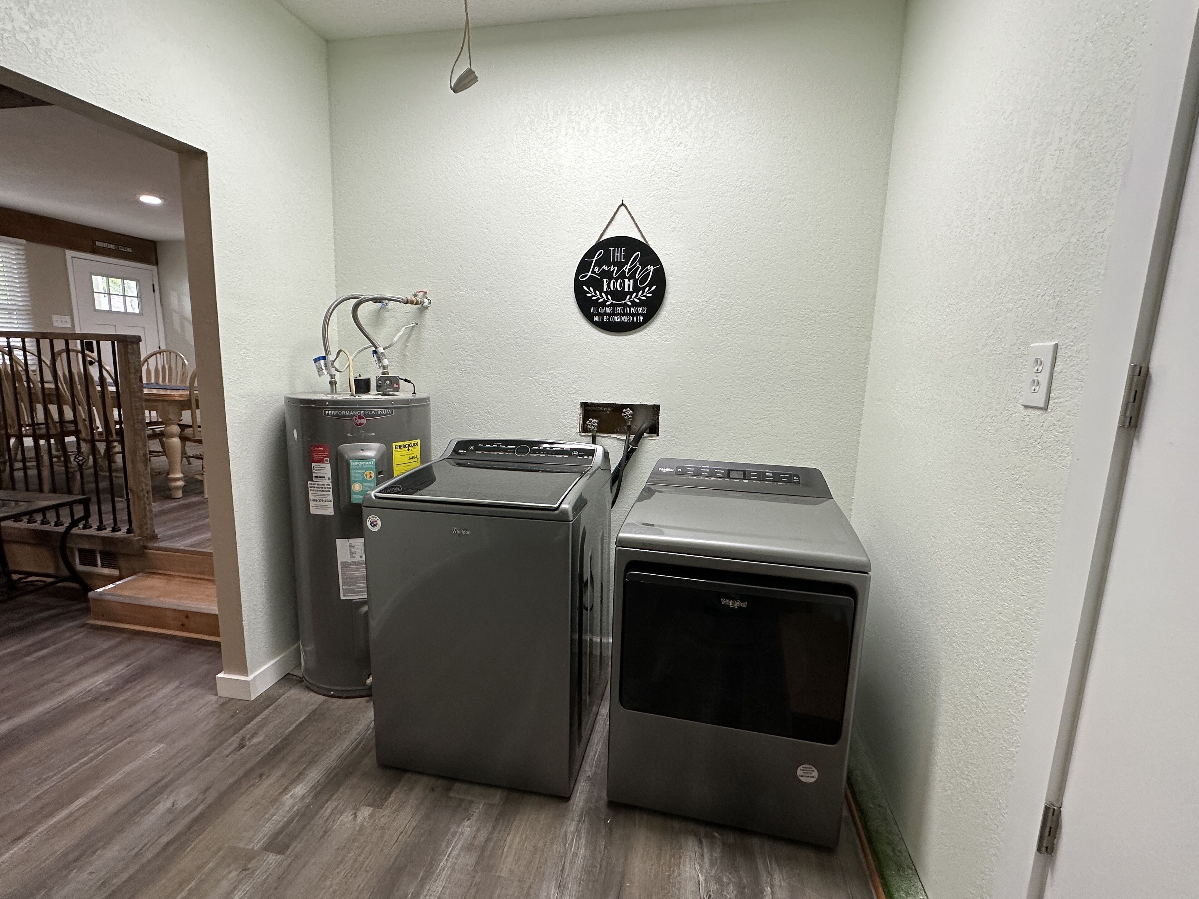 A laundry room with a stacked washer and dryer, a water heater, and a wall-mounted sign.