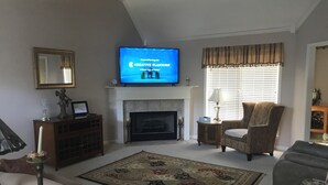 Una sala de estar con chimenea, un televisor montado arriba, un tapete estampado y dos sillones.