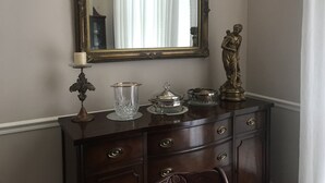 Un aparador de madera oscura con un espejo grande y ornamentado, una pequeña estatua y varios objetos decorativos.