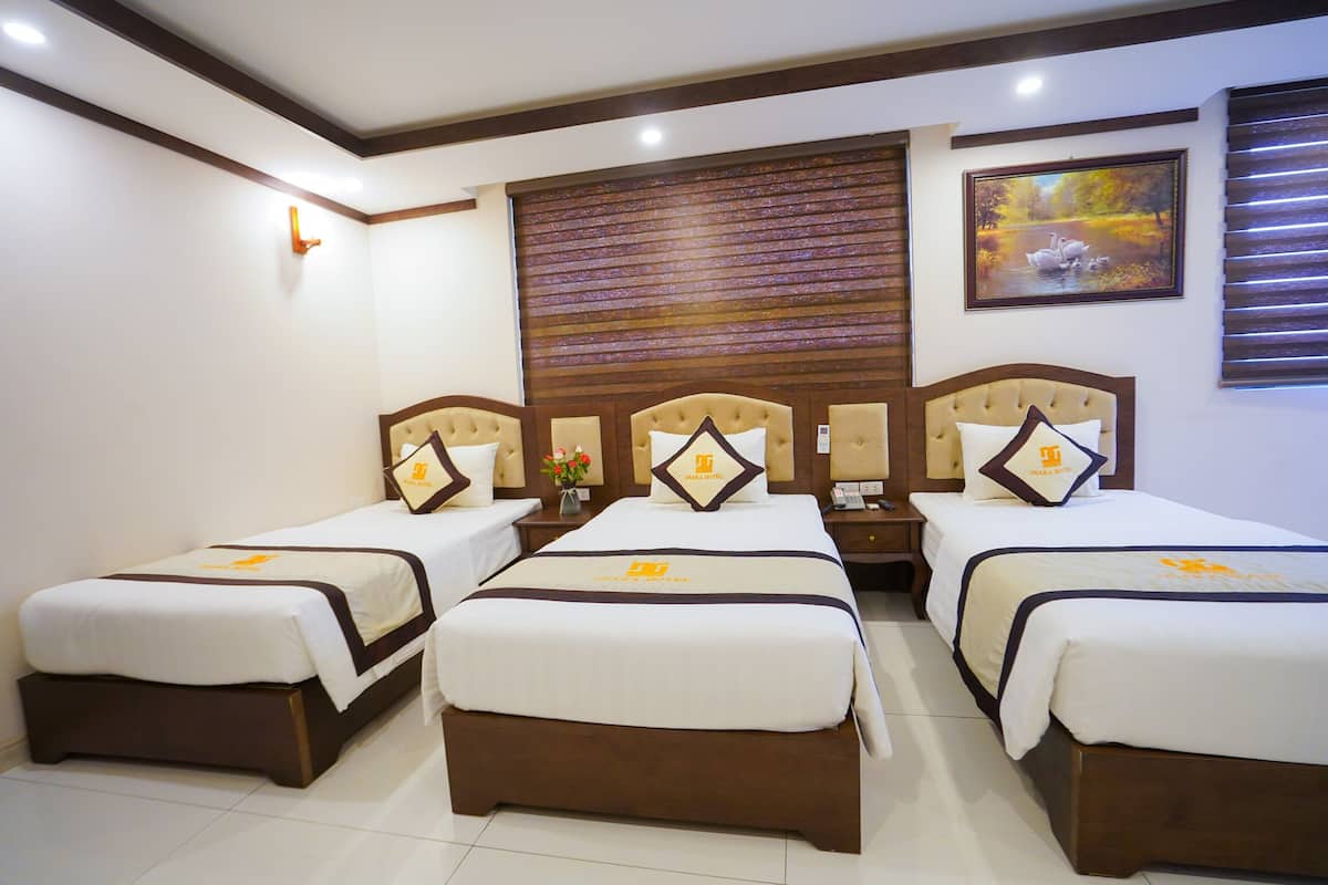 A hotel room with three beds, a wooden headboard, a painting, and a clock on the wall.