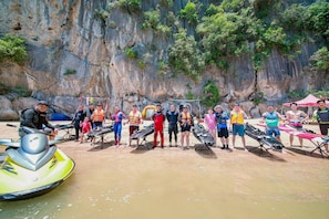 Un groupe de personnes se trouve sur une plage de sable, avec un jet ski et un kayak, entouré de falaises.