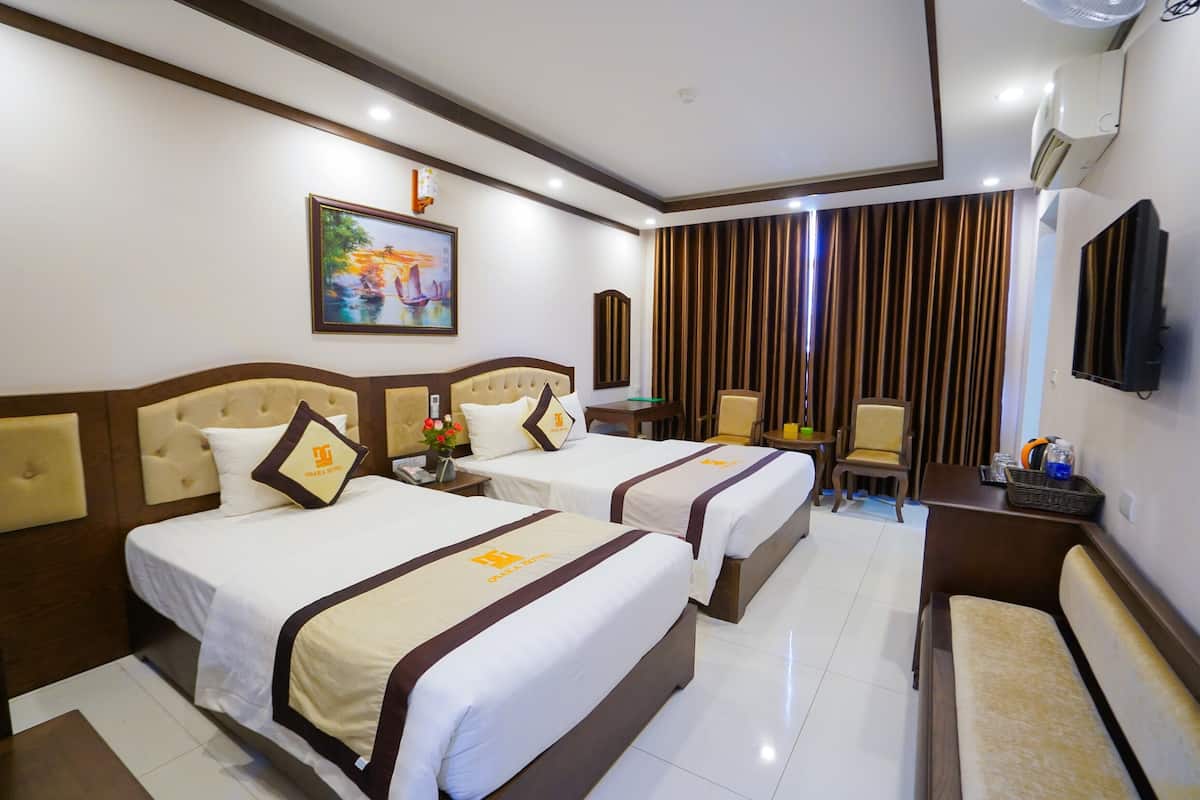 A hotel room with two beds, a desk, a chair, a TV, and a painting on the wall.