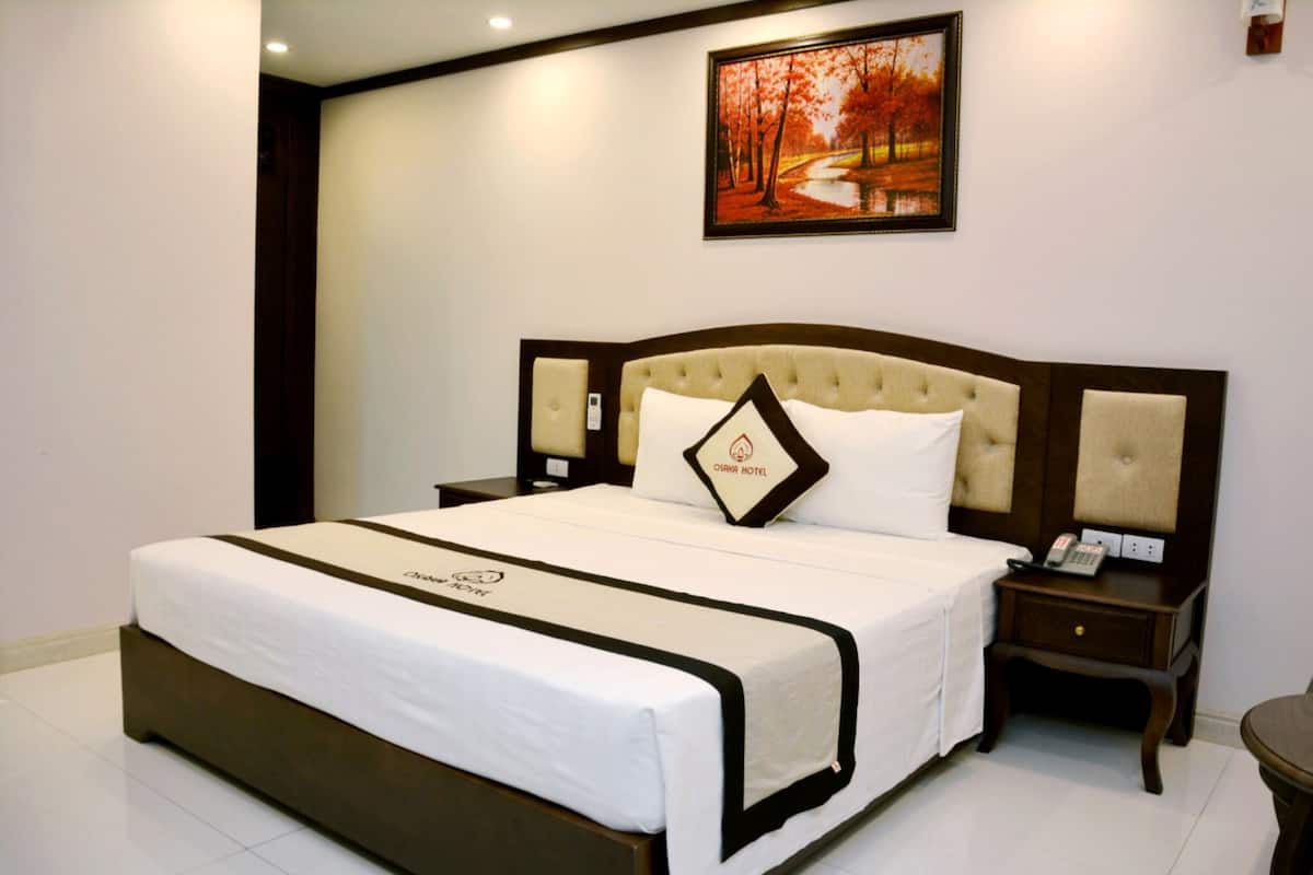 A neatly made bed with a headboard, a bedside table with a lamp, and a framed picture on the wall.