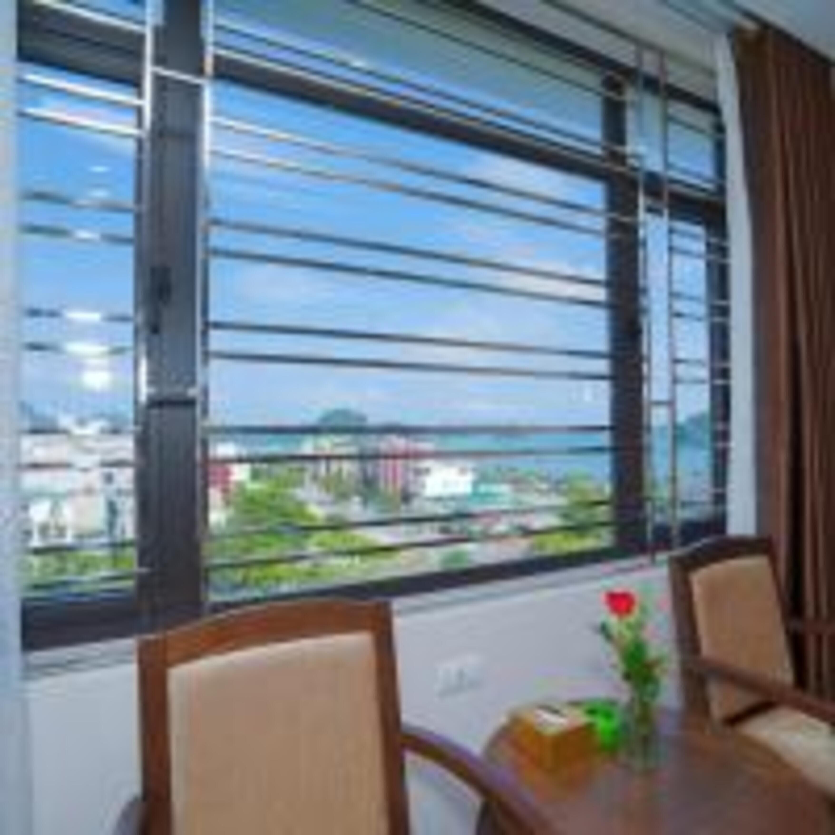 A hotel room with a large window, a dining table with chairs, and a vase with a flower.