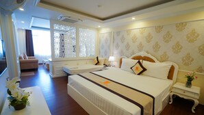 Une chambre d’hôtel avec un grand lit, un plus petit lit, un canapé, un bureau et une fenêtre agrémentée de paravents décoratifs.