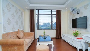 Un salon avec un canapé, une table basse, un téléviseur et une fenêtre avec des rideaux.