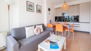 A modern living room with a grey sofa, a white coffee table, and a dining area with orange chairs.