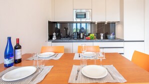 A modern kitchen with a microwave, stove, and various appliances. There is a dining table set with plates, glasses, and cutlery.