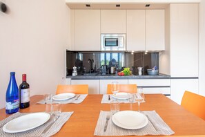 A modern kitchen with a microwave, stove, and various appliances. There is a dining table set with plates, glasses, and cutlery.