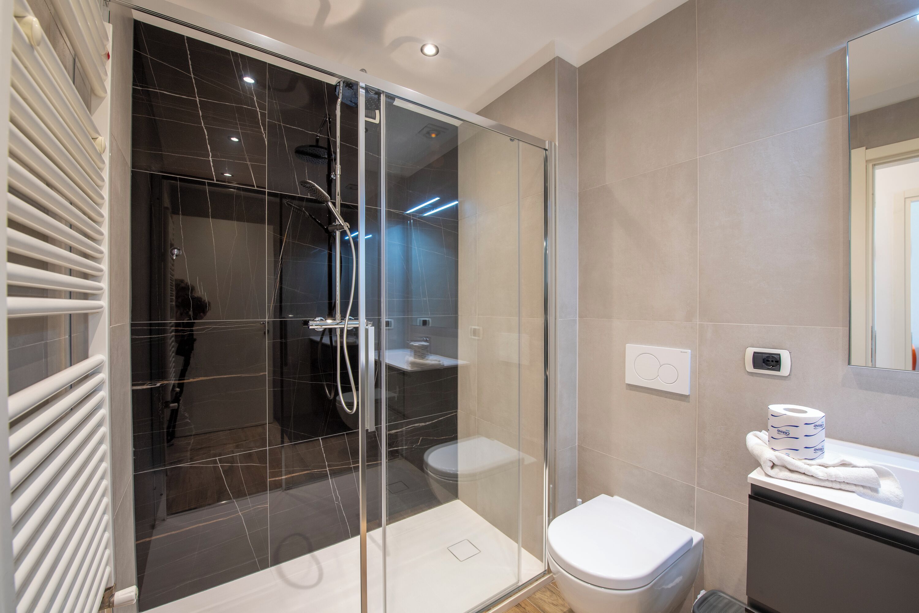 A modern bathroom with a glass-enclosed shower, a white toilet, and a vanity with a towel.