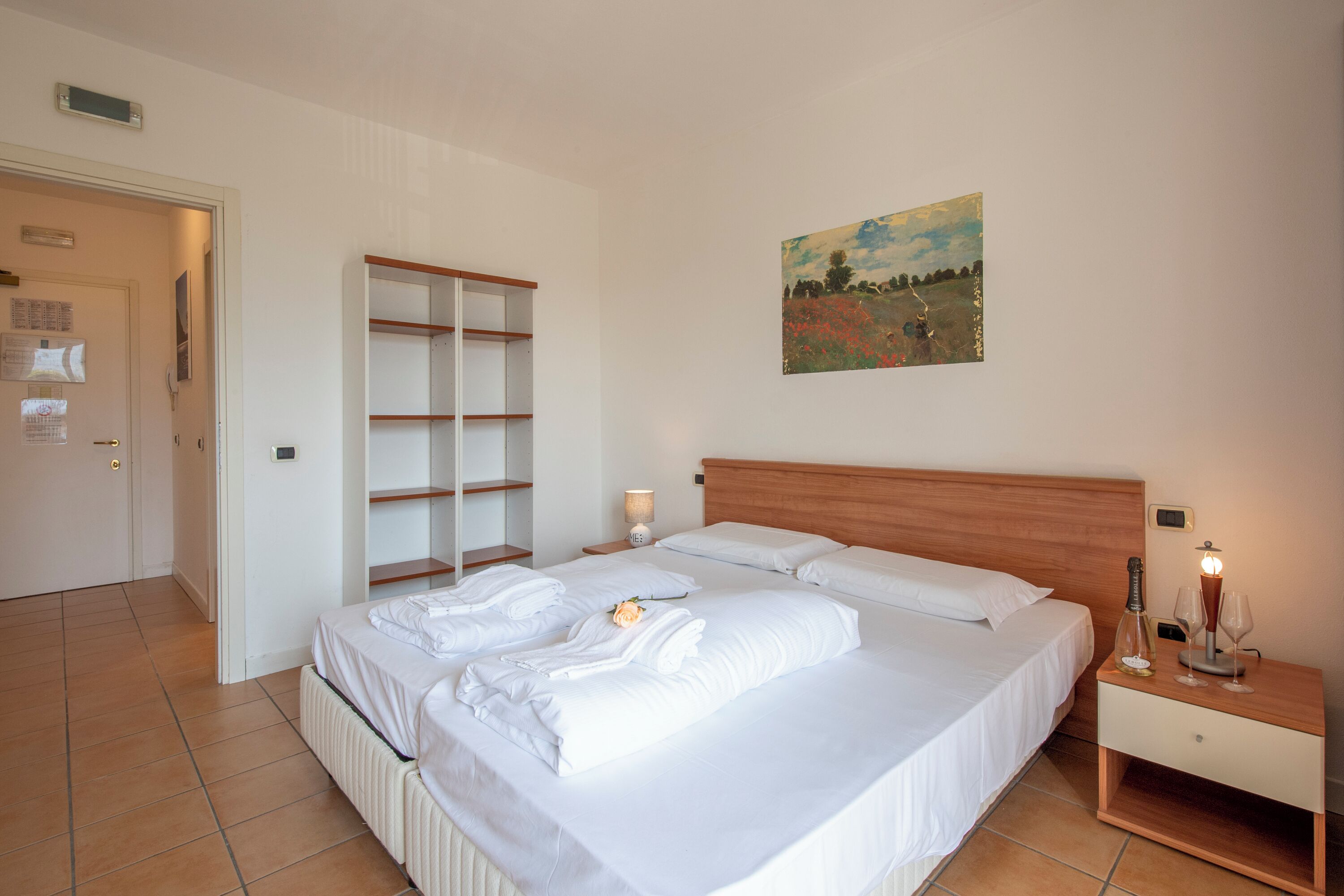 Ein ordentlich gemachtes Bett mit weißen Leinentüchern, einem Holz-Kopfteil und einem Nachttisch mit Lampe und Flasche.