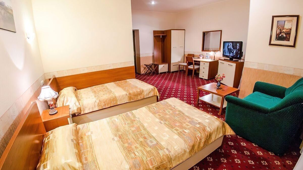 Habitación de hotel con dos camas, un escritorio, una silla, un televisor y un sofá verde.
