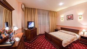 A hotel room with a bed, a television, a desk with a lamp, and a dresser.