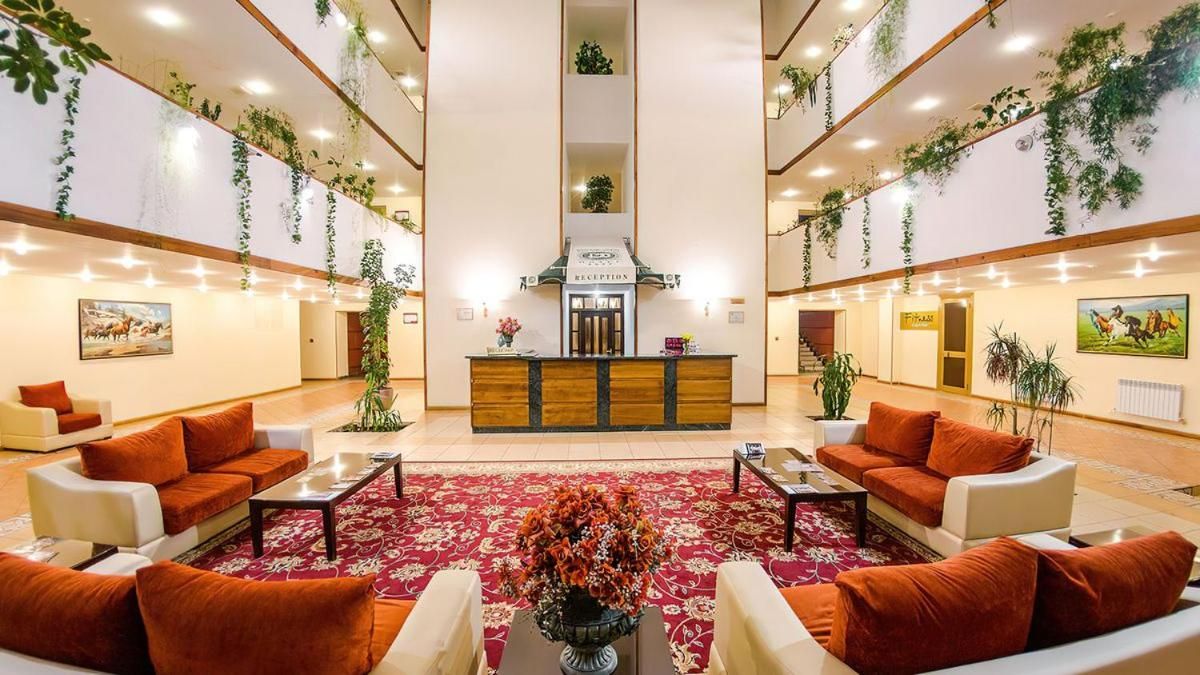 A hotel lobby with a reception desk, sofas, a red carpet, and hanging plants.