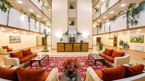 A hotel lobby with a reception desk, sofas, a red carpet, and hanging plants.