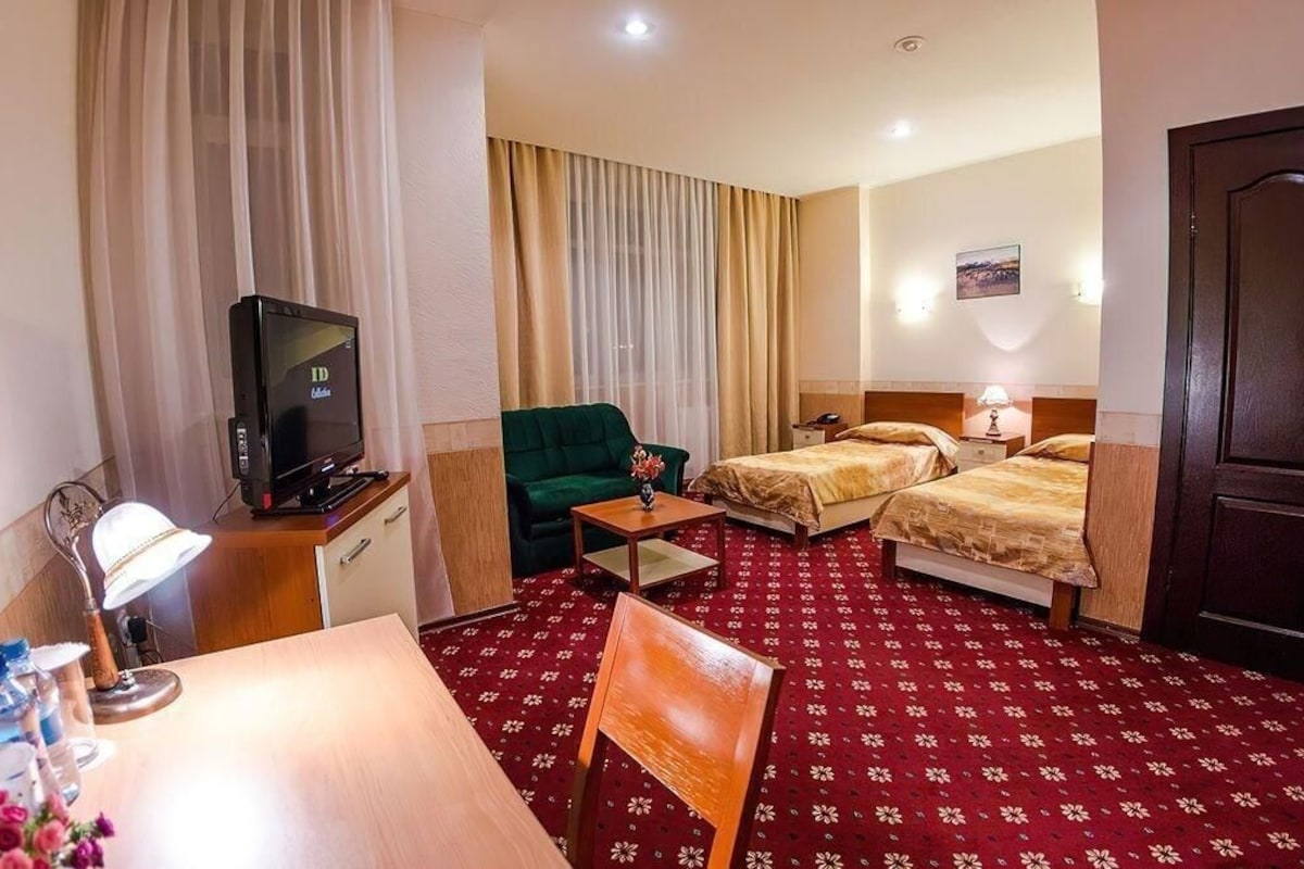 Habitación de hotel con televisión, dos camas, escritorio con lámpara, una silla y alfombra roja.