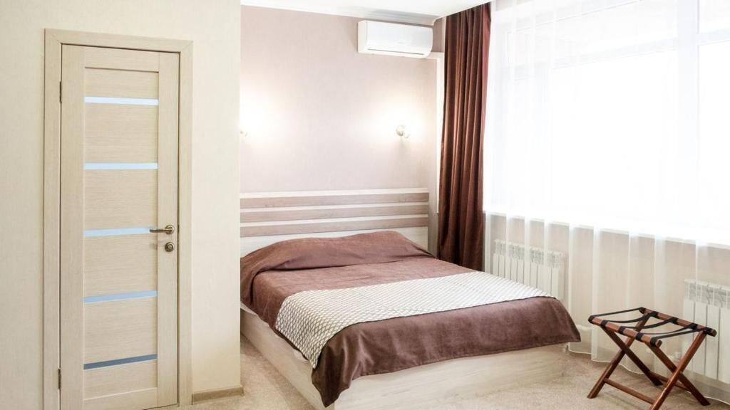 Un dormitorio con cama, un radiador, una ventana con cortinas y una puerta con interruptor de luz.