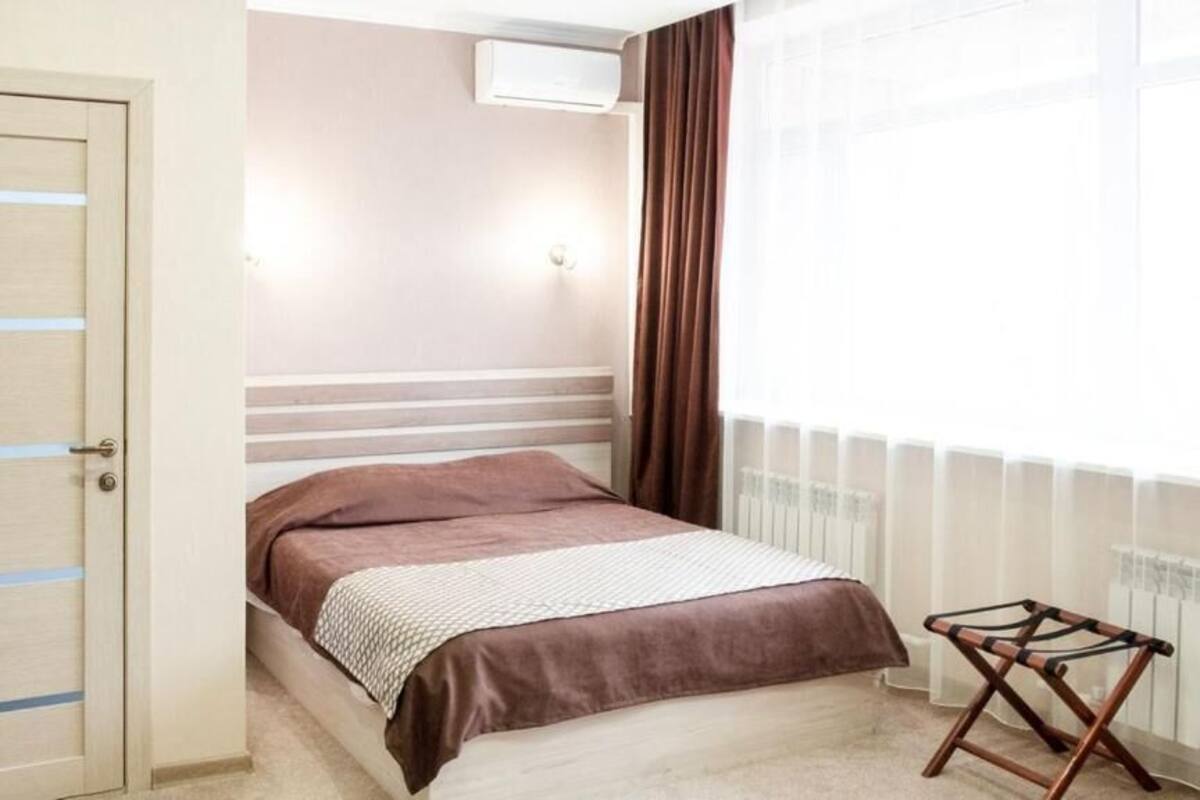 Quarto com cama, radiador, janela com cortinas e porta com interruptor de luz.