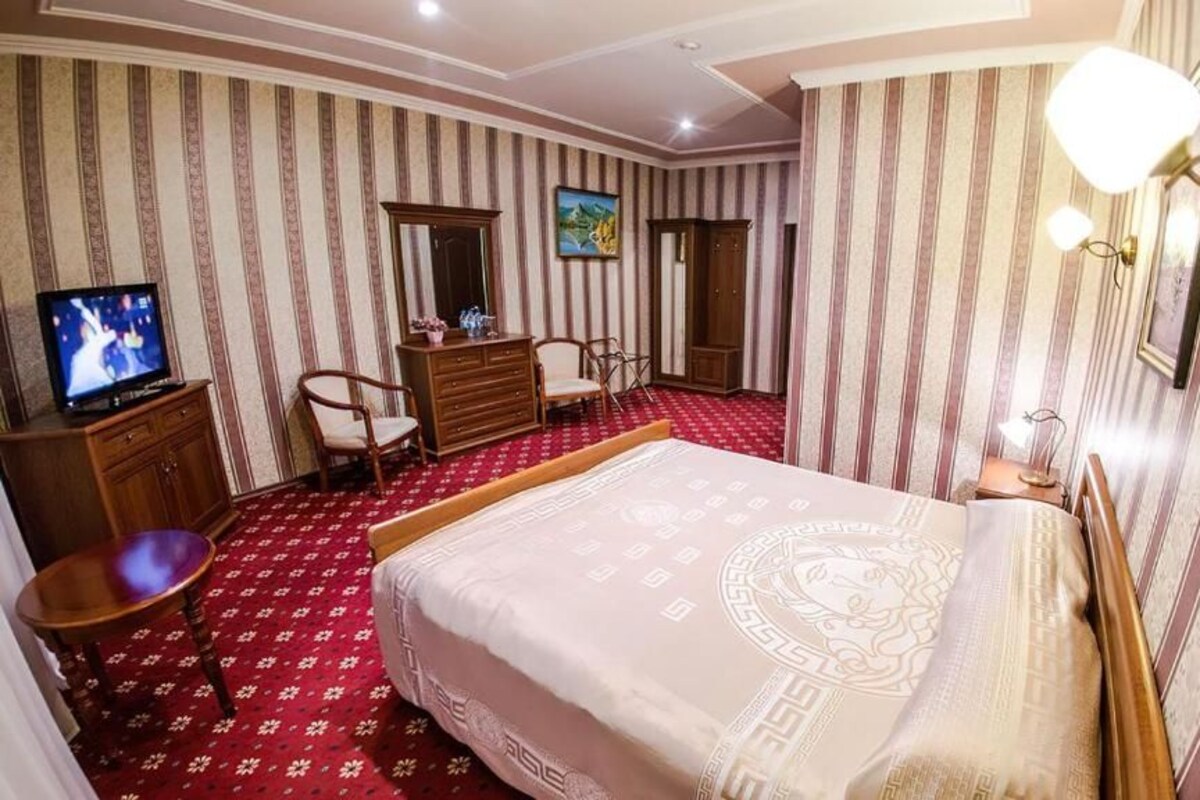 A hotel room with a large bed, a television, a desk, and a wardrobe.