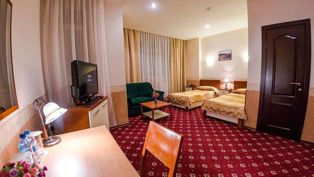 Habitación de hotel con televisión, dos camas, escritorio con lámpara, una silla y alfombra roja.