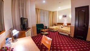 Habitación de hotel con televisión, dos camas, escritorio con lámpara, una silla y alfombra roja.