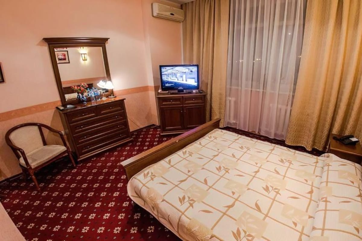 A hotel room with a bed, a dresser, a television, a chair, and a window with curtains.
