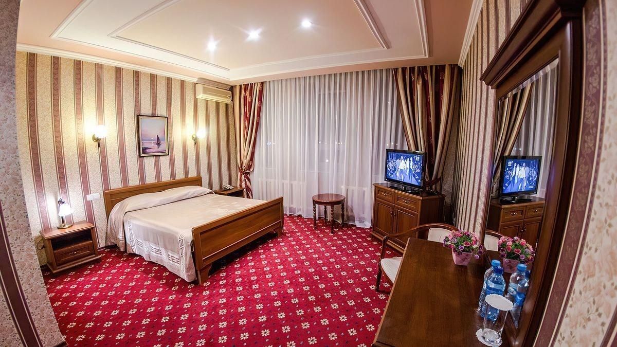 A hotel room with a bed, a TV, a desk with a chair, a small table, and a mirror.