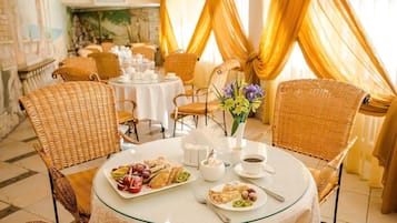 A dining area with wicker chairs, round tables, and a vase with flowers.