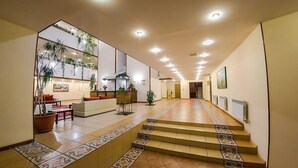 A hotel lobby with a reception desk, seating area, staircase, and potted plants. - Reikartz Karaganda (Karagandy)