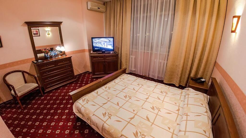 Habitación de hotel con cama, cómoda, televisor, silla y ventana con cortinas.