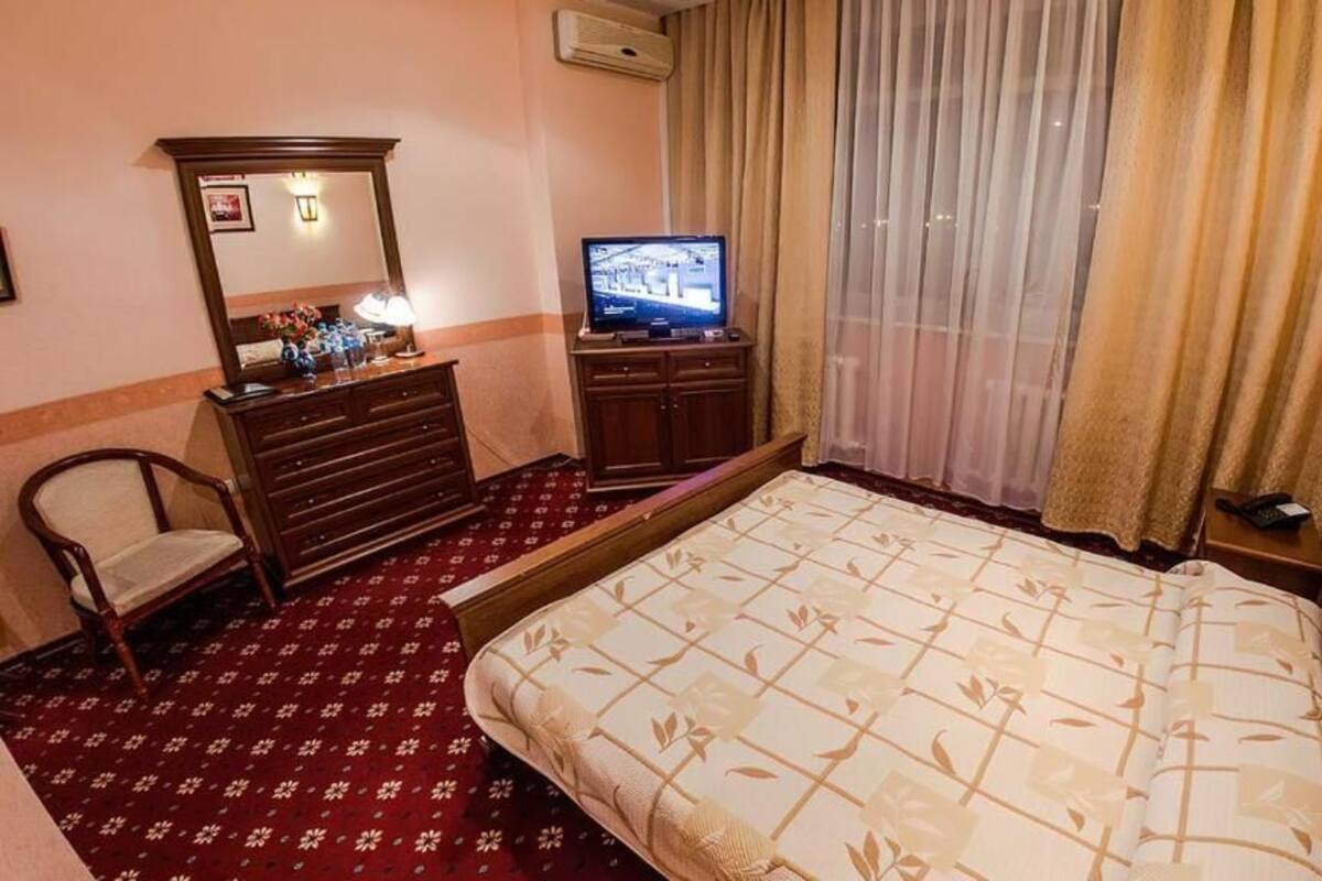 Quarto de hotel com cama, penteadeira, televisão, cadeira e janela com cortinas.