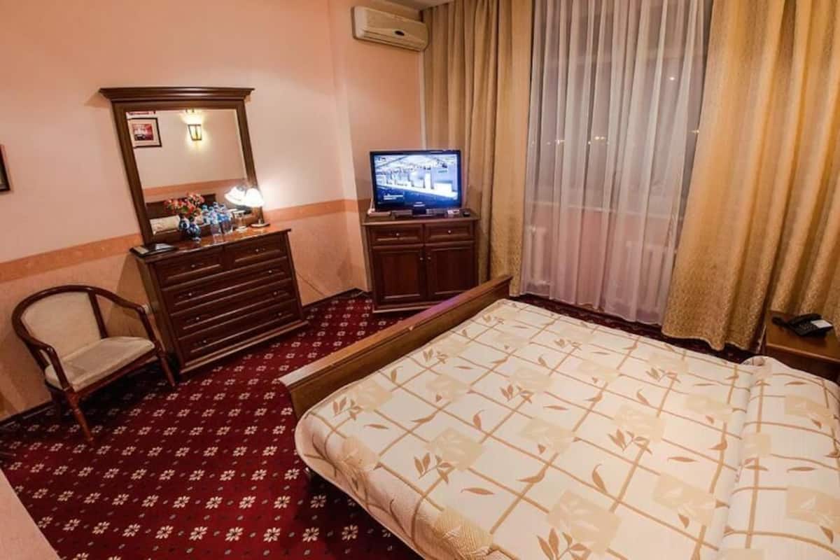 Habitación de hotel con cama, cómoda, televisor, silla y ventana con cortinas.