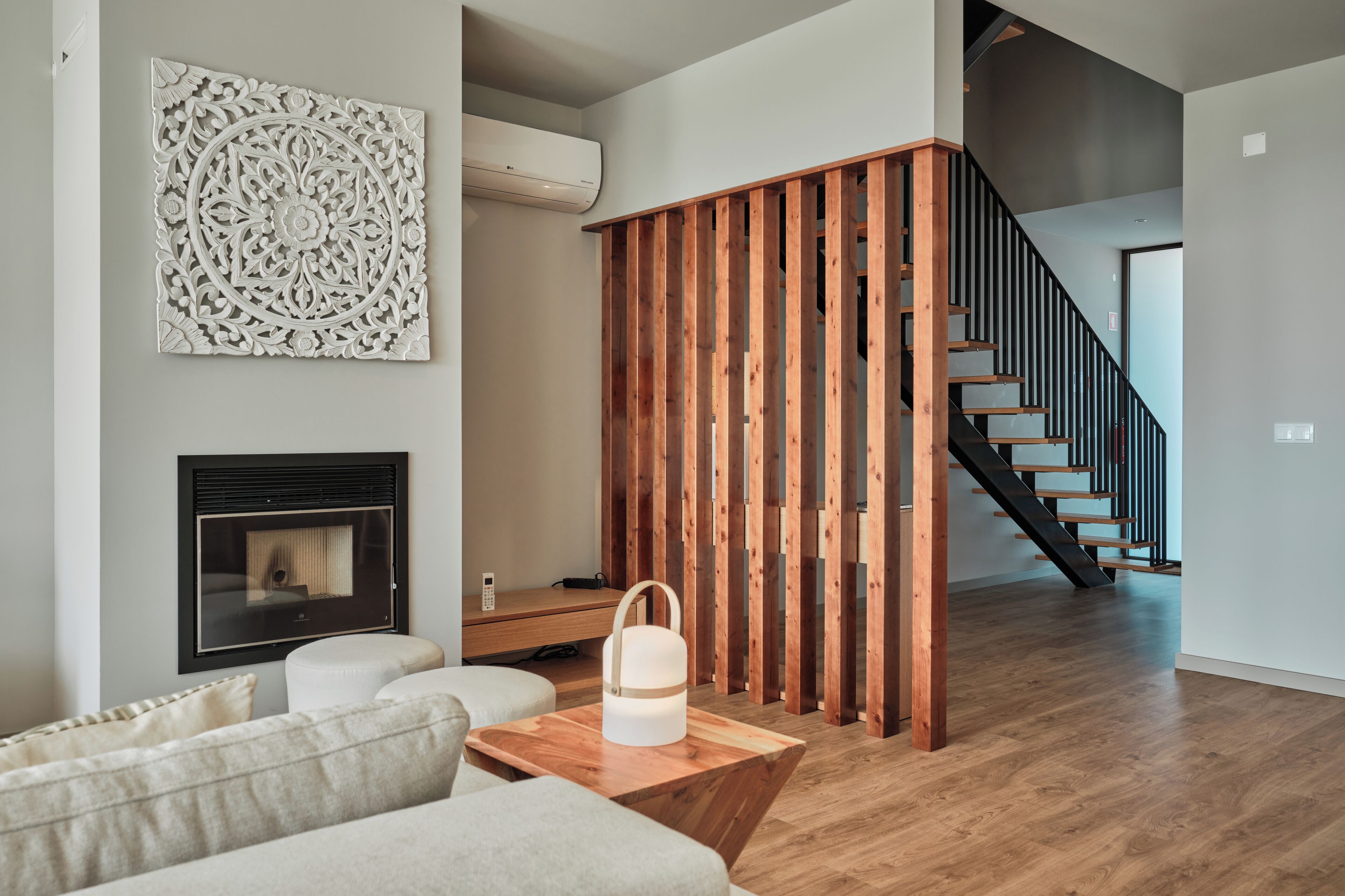 Un salon moderne doté d’une cheminée, d’une cloison en bois et d’un escalier menant à un autre niveau.