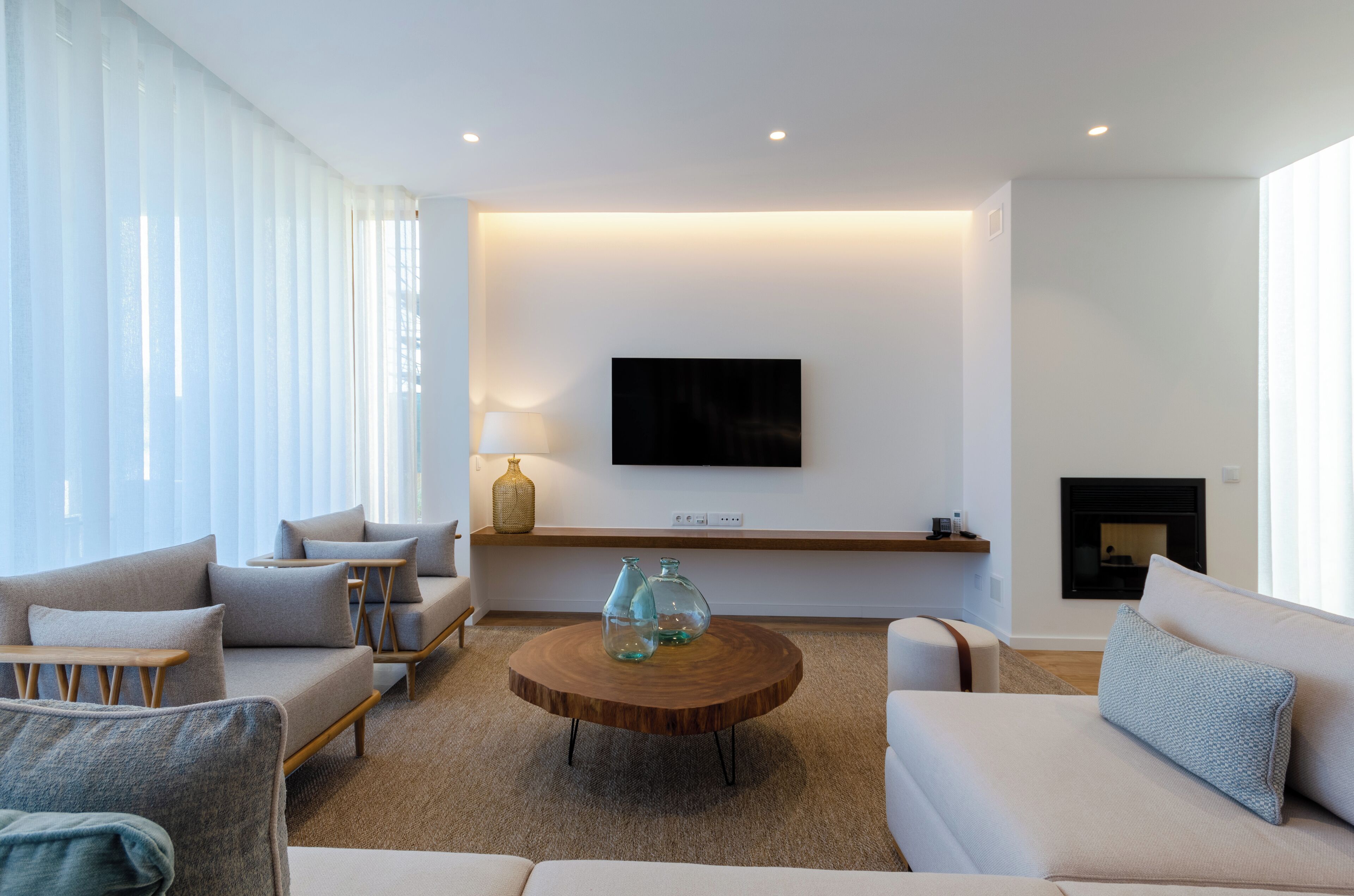 A modern living room with a round coffee table, sofas, a TV mounted on the wall, and a fireplace.