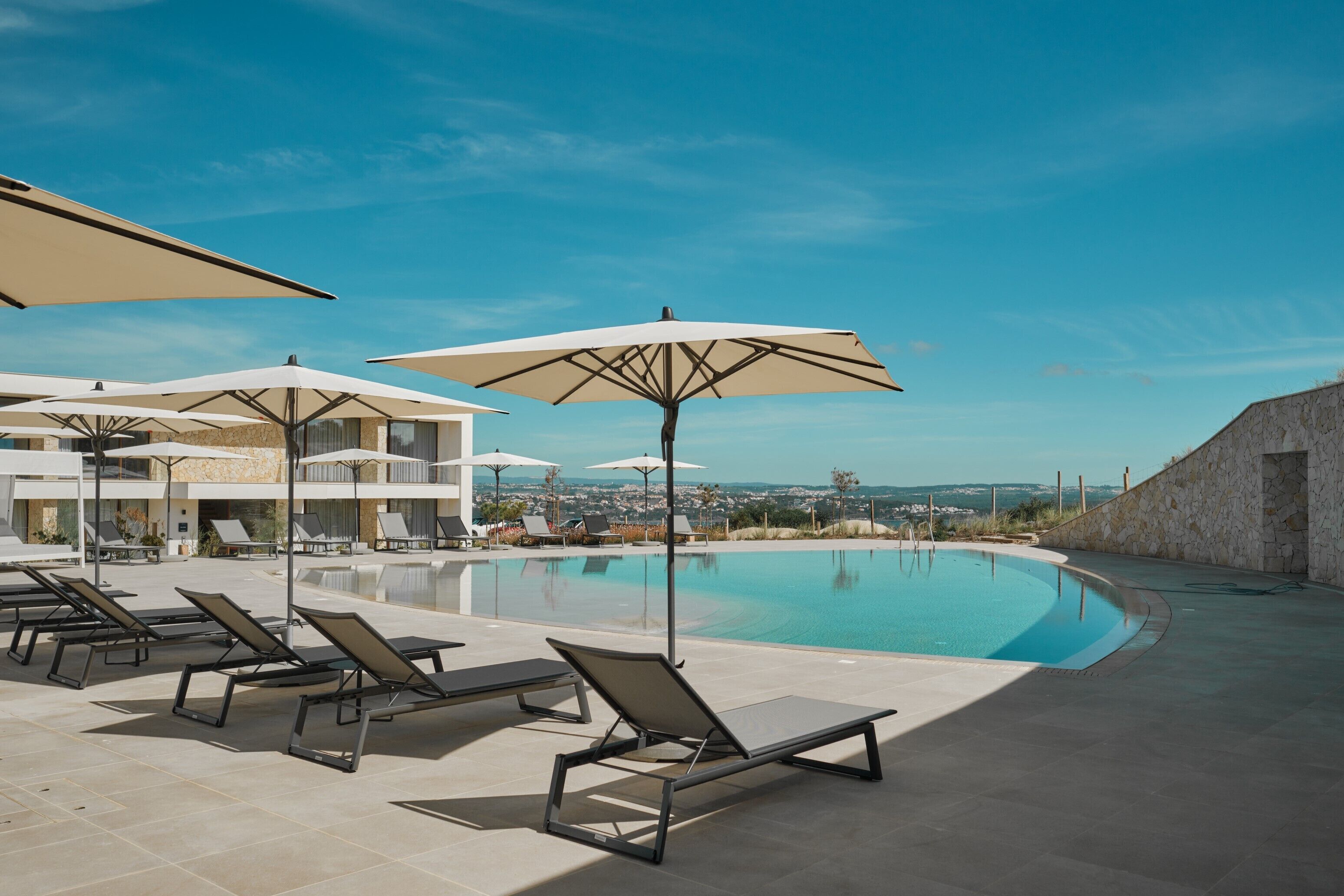 Zona de piscina con sillones y sombrillas, cielo despejado y vista del paisaje.