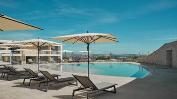 Zona de piscina con sillones y sombrillas, cielo despejado y vista del paisaje.